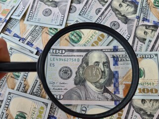 Coin of Russian ruble with magnifying glass against background of dollars