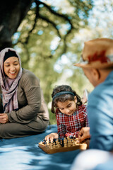 Small Muslim girl plays chess while spending spring day with her parents in nature.