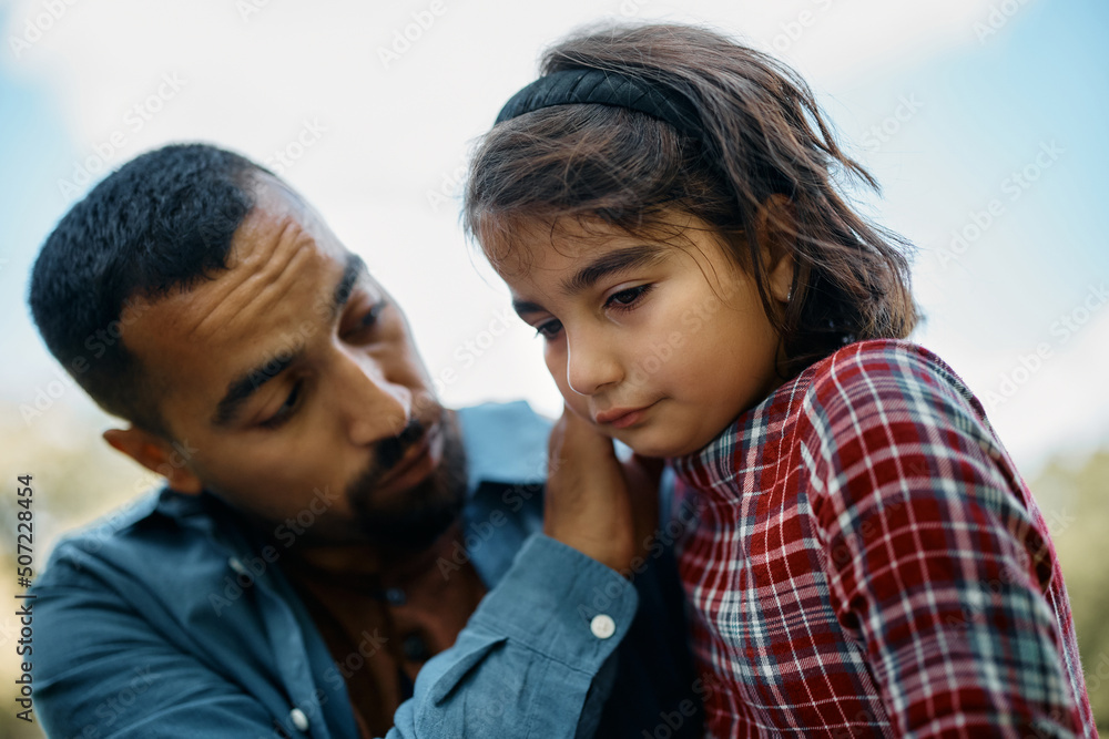 Wall mural Muslim little girl feels sad while father is trying to comfort her in nature.