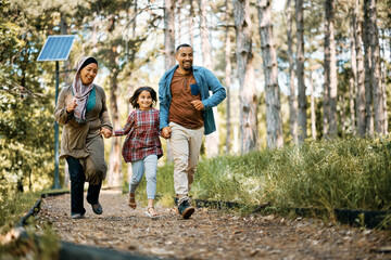 Playful Muslim family has fun while holding hands and running in nature.