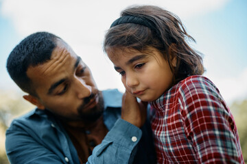 Muslim little girl feels sad while father is trying to comfort her in nature.
