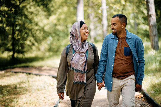 Happy Middle Eastern couple holding hands while walking through park.