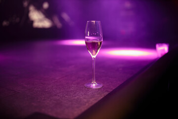 a glass of champagne stands on a stage illuminated with purple and pink lights. a glass of champagne on stage during a concert.