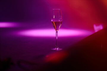 a glass of champagne stands on a stage illuminated with purple and pink lights. a glass of champagne on stage during a concert.
