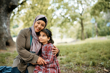 Embraced Muslim mother and daughter enjoy in day together in park.