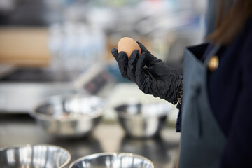 a chef in black gloves holds a chicken egg in his hand, against the background of kitchen utensils
