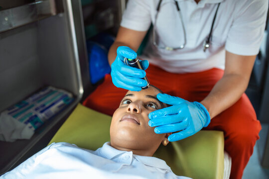 Close-up Portrait Shot Of A Serious And Focused Paramedic In An Ambulance Vehicle With An Injured Patient. Emergency Medical Technician Uses Stethoscope To Monitor The Condition