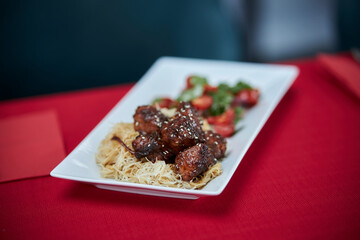 served table, sweet and sour chicken with sesame seeds on a white plate and glasses of champagne