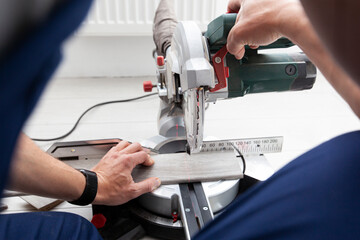 A worker cuts a skirting board made of fibreboard with a miter saw