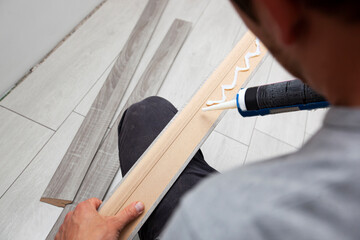A worker applies glue to a baseboard before installing it on the floor - obrazy, fototapety, plakaty