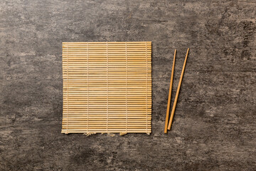 Two chopsticks and bamboo mat on cement background. Top view, copy space