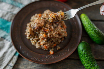 Buckwheat porridge on a fork, close-up A plate of buckwheat porridge with carrots and meat. Fork, cucumber, tomato