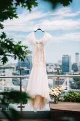 beige handmade casual wedding dress hang on the glass veranda city view
bride's morning 
