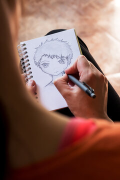 look over the shoulder, as a girl draws a face with a pencil