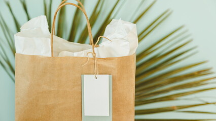 Craft recycle paper bag with white tag against green palm leaf. Elegant modern template for...