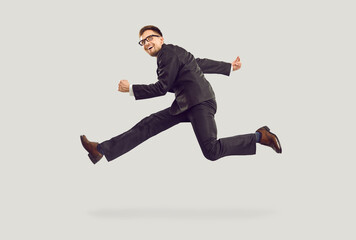 Crazy excited young businessman in black suit running and jumping isolated on gray background. Side...