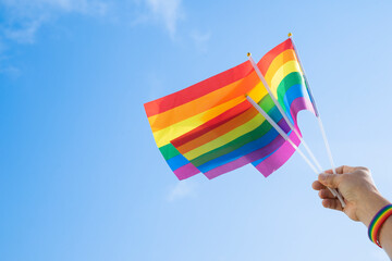 man's hand wears LGBT rainbow wristband is waving LGBT rainbow flags on background blue sky(selective focus), concept for LGBTQ+ equality movement community