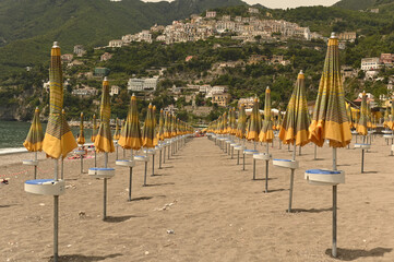 Yellow beach umbrellas from the sun on a sandy beach on a background of mountains and sea