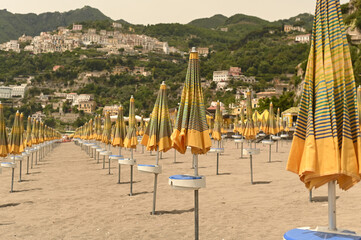 Yellow beach umbrellas from the sun on a sandy beach on a background of mountains and sea