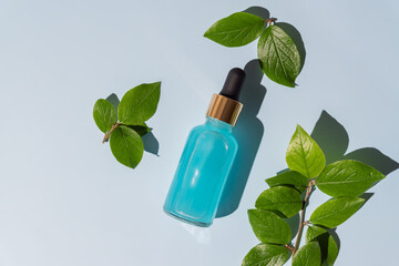 Dropper glass Bottle Mock-Up. Fece treatment and spa. Natural beauty products. Beauty serum, skin care blank glass bottle. Blue background with green tropical leaves.