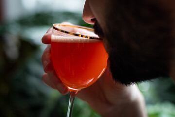 Man drinking red cocktail in nick and nora glass with green background