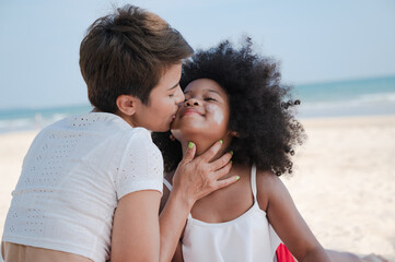 Mother kiss African American daughter on the beach