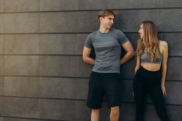 Obraz na płótnie Canvas Portrait of fitness couple smiling and looking away. Cheerful mature man and beautiful woman laughing while resting after running. Healthy couple leaning against wall with copy space.