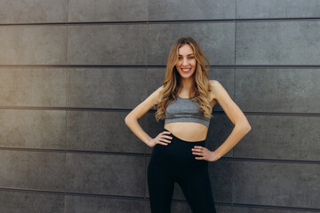 Portrait of beautiful fitness woman smiling and looking at camera isolated on black wall. Happy fit girl on gray wall with copy space.