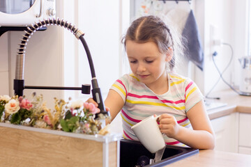 Pretty little girl helping parents to wash dishes in the kitchen at home.