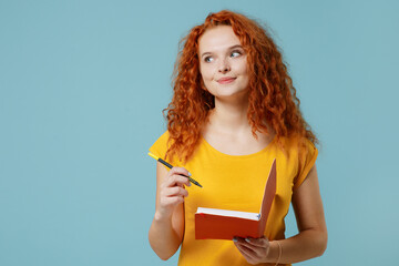Young minded happy redhead woman 20s wearing yellow t-shirt look aside write down thoughts in diary...