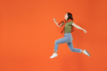 Fototapeta na wymiar Full body side view young hurrying cool fun happy woman 20s wearing khaki t-shirt tied sweater on shoulders jump high run isolated on plain orange background studio portrait. People lifestyle concept.