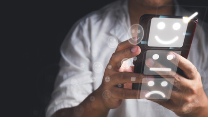 Evaluation and satisfaction concept. The man chooses a smile emotion that is an excellent review with unidentified model of mobile phone. Medium close up shot on black background.