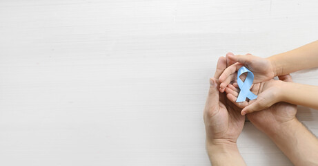World diabetes day. Child and father are holding blue ribbon on white background. Hands close up. 14 november. November Blue. Copy space. Top view banner