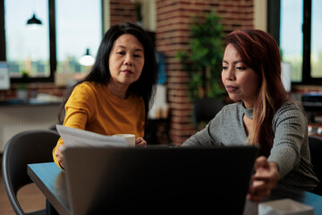 Asian entrepreneurs working at marketing project analyzing statistics on laptop computer brainstorming ideas during business meeting in startup office. Executive managers collaborating together