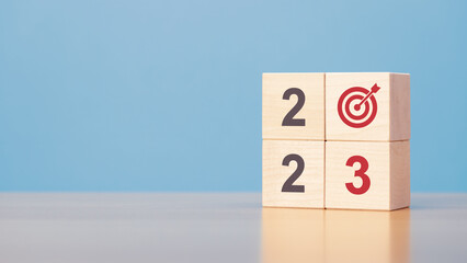 New year 2023 goal. Wooden blocks with 2023 and target icon on wooden table blue background copy space.