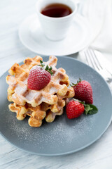 Viennese waffles with strawberries on a gray plate, a cup of coffee on a light table.