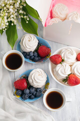 On a bright table are cups of tea, plates with marshmallows, strawberries and blueberries, a bouquet of lilies of the valley. Tea party concept.