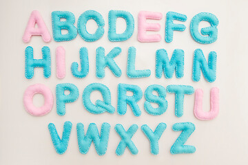 Full alphabet in capital letters made from stuffed felt on wooden floor background. Toy and implement for preschool and primary school kids learn to read. Montessori colors.