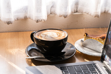 Hot coffee latte with latte art milk foam in cup mug and Homemade chocolate cake and laptop computer on wood desk on top view. As breakfast In a coffee shop at the cafe,during business work concept