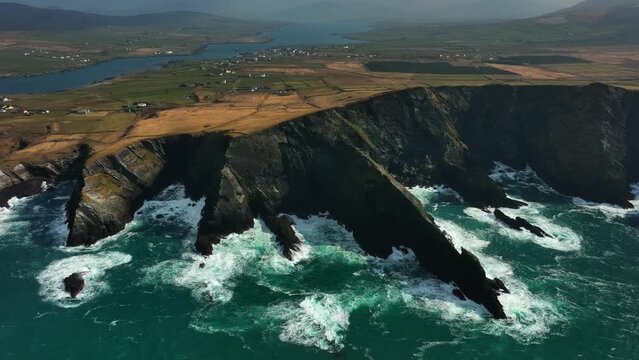 Portmagee Cliffs, Kerry, Ireland, March 2022. Drone tracks south along the rugged coastline on the Iveragh Peninsula with Portmagee town and Valentia Island in the distance.