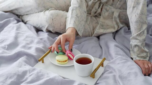 Woman have breakfast in bed. Eat colorful macarons and drink coffee or tea