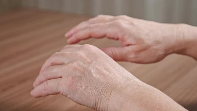 Old woman trembling hands due to Parkinson disease. Lady with shakiness holds wrinkled hands over table. Elderly female hands tremor closeup