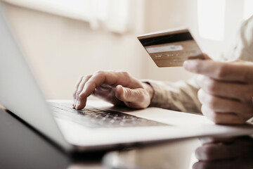 Man hand holding credit card and using laptop at home, Businessman or entrepreneur working, Online shopping, e-commerce, internet banking, spending money, working from home concept