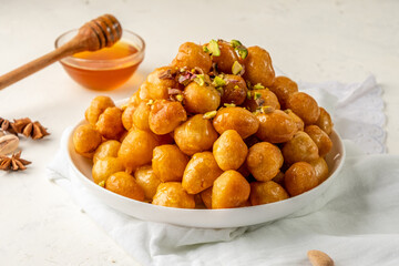 luqaimat or lokma Arabic dessert, fried dough in the shape of a ball, in a white plate, decorated with nuts, on a honey background, white background.