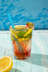 A glass with a refreshing summer drink with strawberries and lemon on a blue background.