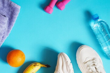 Purple towel, healthy food, clear water bottle, dumbbells and sneakers flat lay photography. Blue sport background for design website. Mockup, free space for text