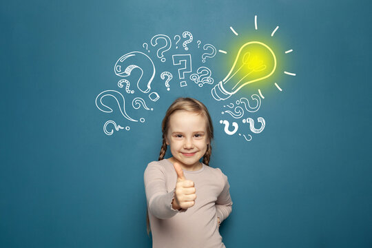Portrait of a cute little girl showing thumb up and standing near a blue wall with a question marks and a yellow light bulb drawn above his head