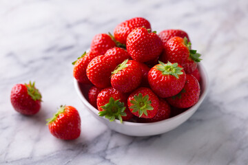 Strawberries in white bowl. Marble background. Close up.