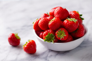 Fresh strawberries in white bowl. Marble background. Close up.