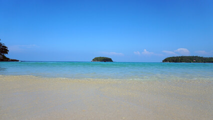 A lonely island in the sea. A Thai fishing boat floats nearby. Clear blue water, snow-white sand. Small clouds in the sea. Palm trees and trees grow on the island. Beautiful Kata beach, Phuket